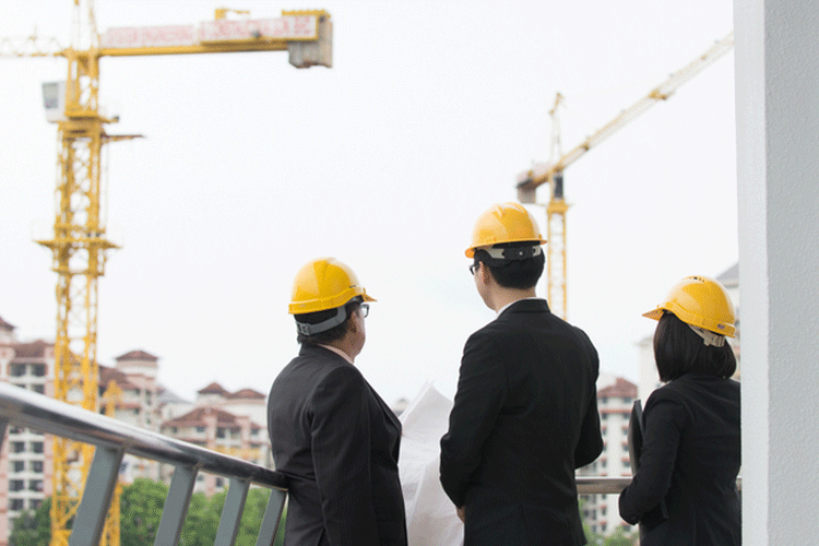 Three professionals in suits on a balcony overlooking construction cranes
