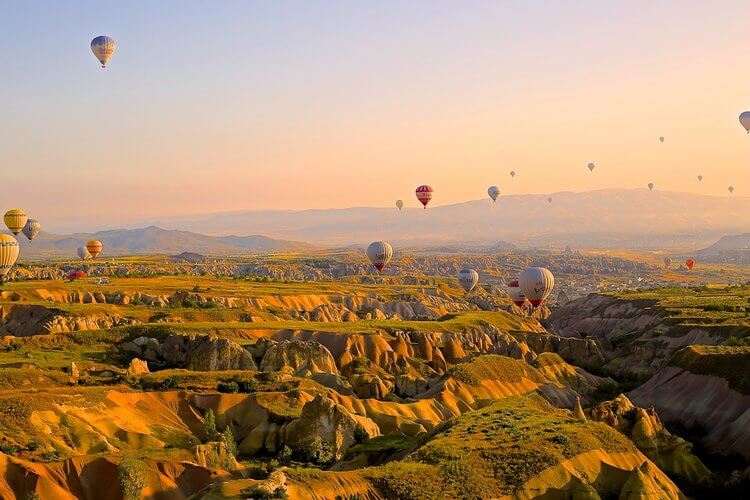 Many hot air balloons soaring above a picturesque valley, creating a colorful spectacle in the sky